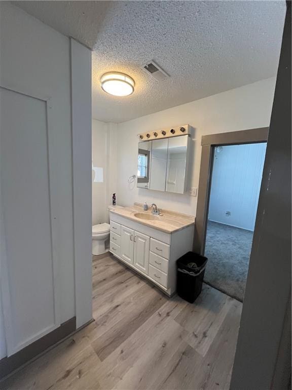 bathroom with toilet, a textured ceiling, visible vents, and wood finished floors