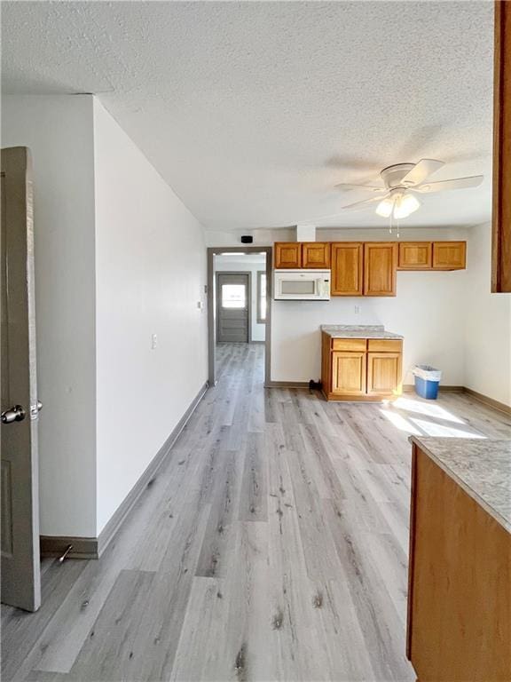 kitchen with light wood-type flooring, white microwave, baseboards, and a textured ceiling