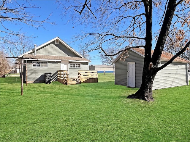 exterior space with a shingled roof, a lawn, an outdoor structure, and a wooden deck