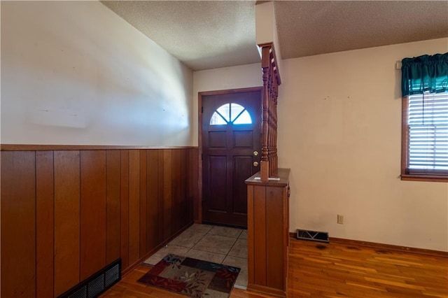 foyer with a wainscoted wall, plenty of natural light, a textured ceiling, and visible vents