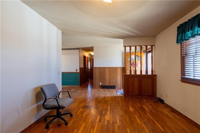 unfurnished room featuring visible vents, a textured ceiling, wood finished floors, and wainscoting