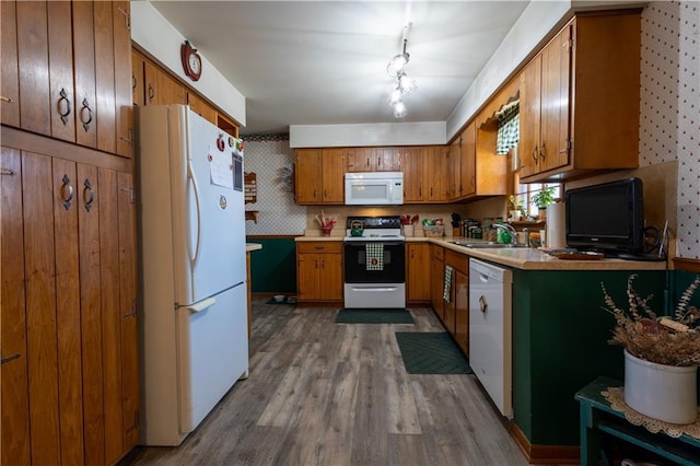 kitchen with white appliances, brown cabinetry, dark wood-style flooring, a sink, and light countertops