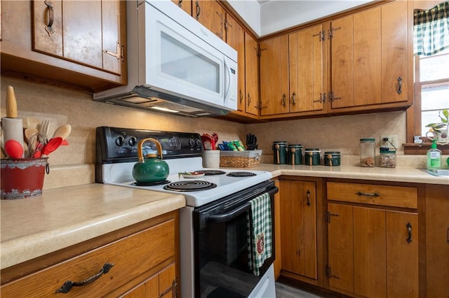 kitchen with brown cabinets, white microwave, light countertops, and electric stove