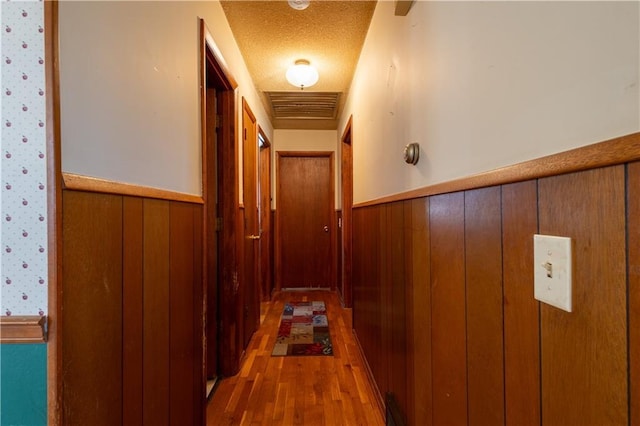 hall featuring a wainscoted wall, visible vents, a textured ceiling, wood finished floors, and wood walls