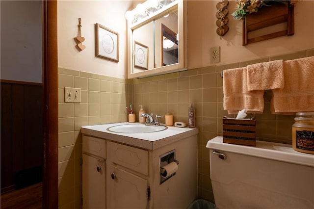 bathroom with wainscoting, vanity, tile walls, and toilet