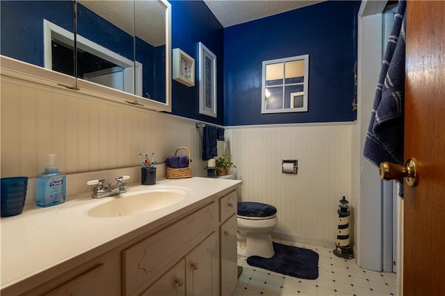 bathroom with a wainscoted wall, toilet, vanity, tile patterned floors, and a textured ceiling