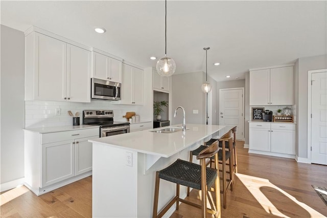 kitchen with appliances with stainless steel finishes, a sink, light wood-style flooring, and decorative backsplash