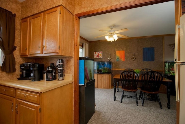 kitchen with ornamental molding, ceiling fan, light countertops, wallpapered walls, and light carpet