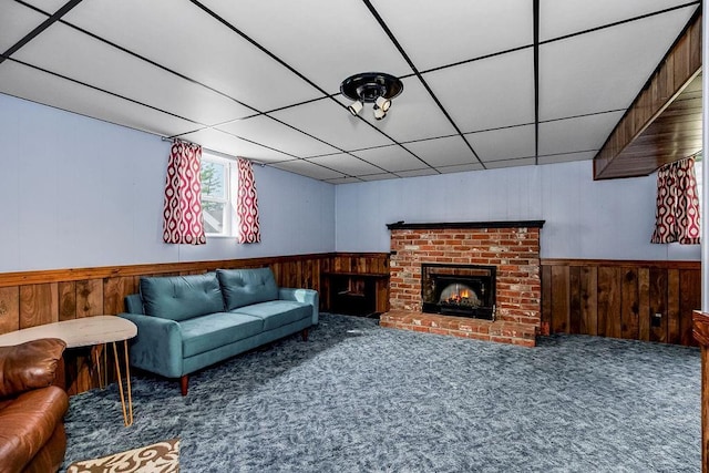 carpeted living room with a paneled ceiling, wood walls, a fireplace, and wainscoting