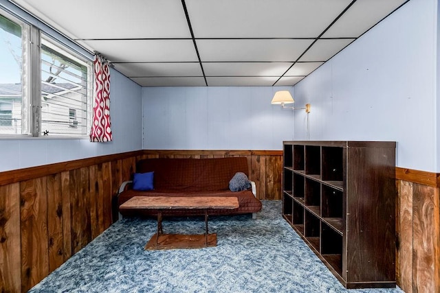 sitting room with a paneled ceiling, wooden walls, carpet flooring, and a wainscoted wall