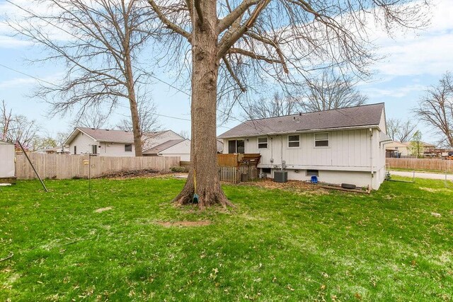 back of house with central air condition unit, fence, and a lawn