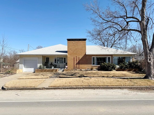 view of front facade with an attached garage, driveway, a chimney, and brick siding