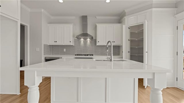 kitchen with a sink, light countertops, wall chimney range hood, backsplash, and crown molding