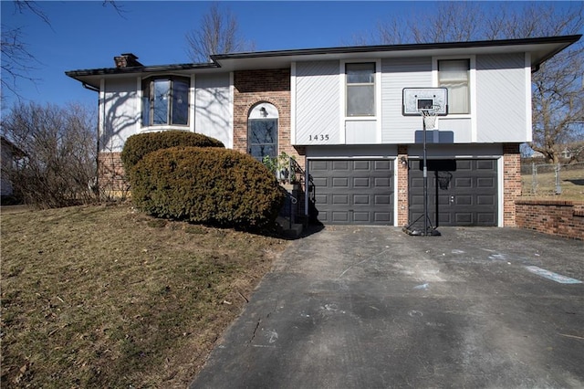 raised ranch with brick siding, a chimney, an attached garage, and aphalt driveway