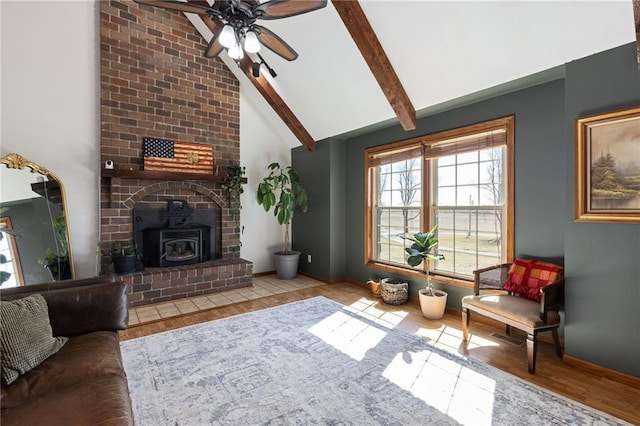 living area featuring vaulted ceiling with beams, baseboards, ceiling fan, a wood stove, and wood finished floors