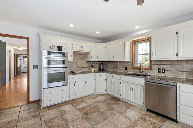 kitchen featuring a sink, tasteful backsplash, white cabinetry, stainless steel appliances, and dark stone counters