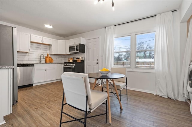 kitchen featuring wood finished floors, appliances with stainless steel finishes, a sink, and decorative backsplash