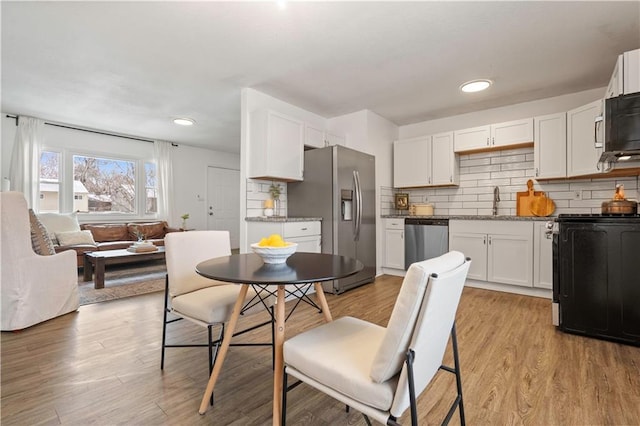 kitchen featuring light wood finished floors, backsplash, appliances with stainless steel finishes, white cabinets, and a sink