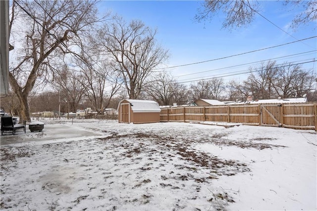 snowy yard with an outbuilding, a gate, fence, and a storage unit