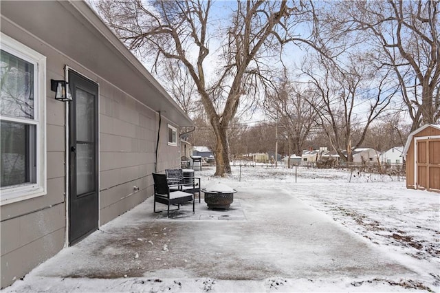 snow covered patio featuring a storage shed, a fire pit, and an outdoor structure