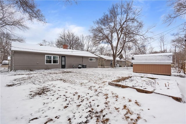 snow covered property featuring a storage unit, a chimney, and an outdoor structure