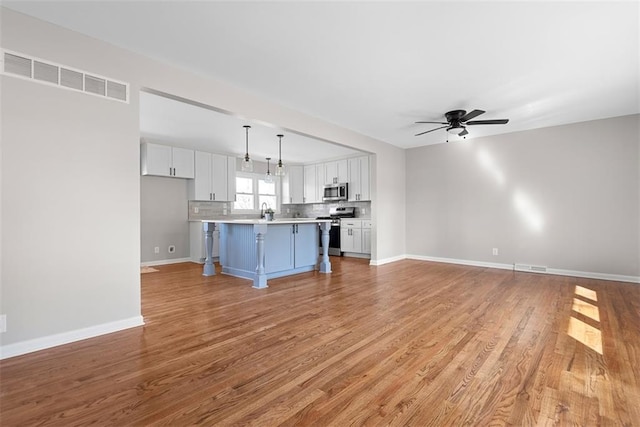 unfurnished living room with light wood-type flooring, baseboards, visible vents, and a ceiling fan