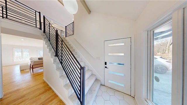 foyer entrance featuring high vaulted ceiling, stairway, beam ceiling, and light wood-style floors