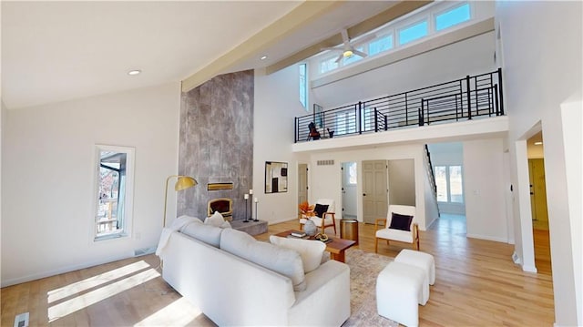 living room with light wood-style floors, a fireplace, high vaulted ceiling, and baseboards