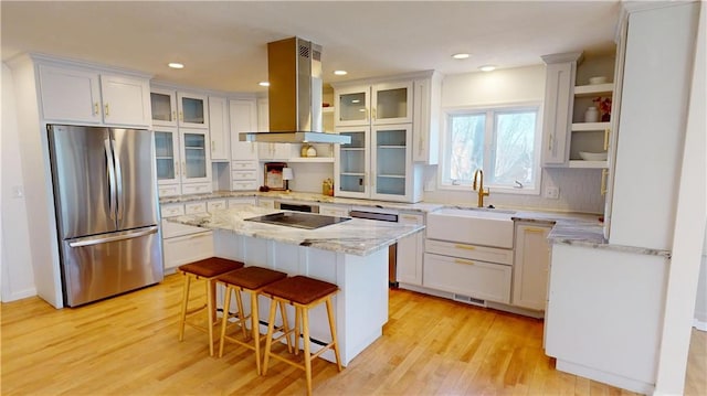 kitchen with a center island, island exhaust hood, appliances with stainless steel finishes, light wood-style floors, and a sink