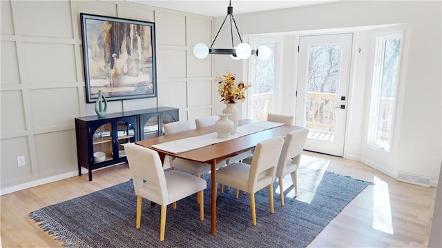 dining area with a notable chandelier, light wood-type flooring, visible vents, and a decorative wall