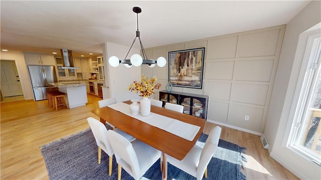 dining room featuring a notable chandelier, a decorative wall, visible vents, and light wood finished floors