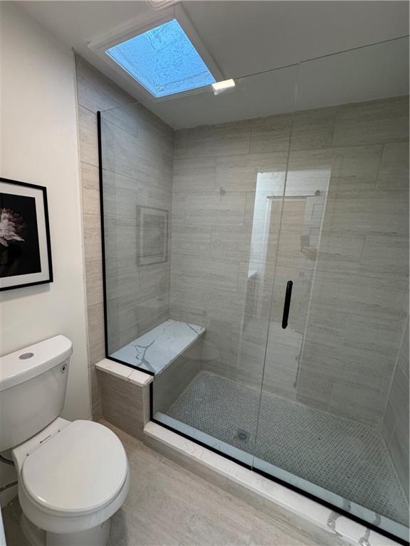 full bath featuring toilet, a skylight, and a stall shower