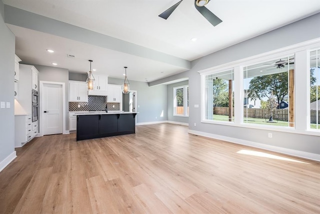 kitchen featuring light countertops, decorative backsplash, open floor plan, white cabinetry, and ceiling fan