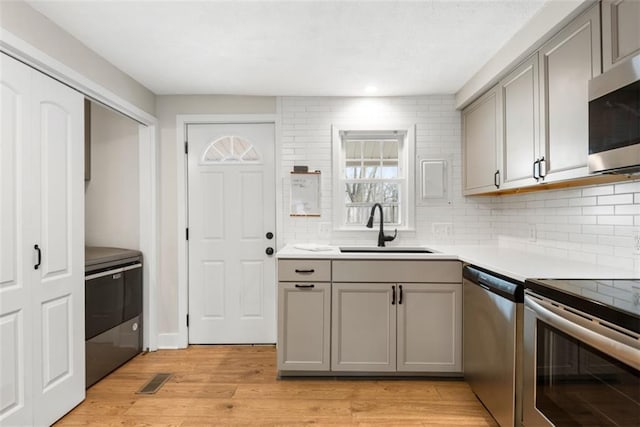 kitchen with appliances with stainless steel finishes, light wood-type flooring, a sink, and gray cabinetry