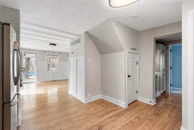 hall with a textured ceiling, light wood-type flooring, visible vents, and baseboards