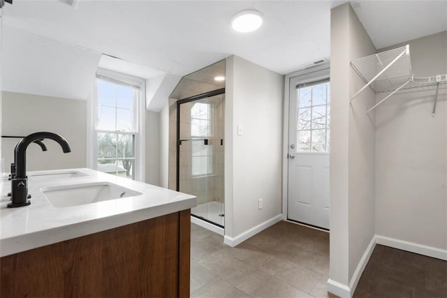 full bathroom featuring double vanity, baseboards, a walk in closet, a shower stall, and a sink