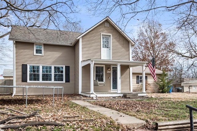 traditional-style house with covered porch, roof with shingles, and fence