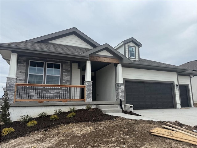 view of front facade featuring covered porch, stone siding, an attached garage, and driveway