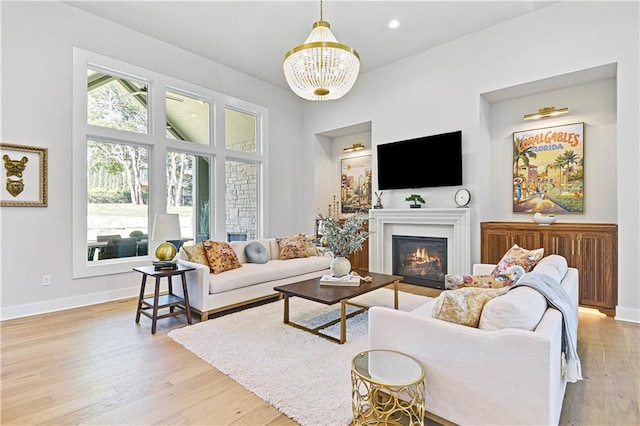 living area with baseboards, a glass covered fireplace, light wood-style floors, a chandelier, and recessed lighting