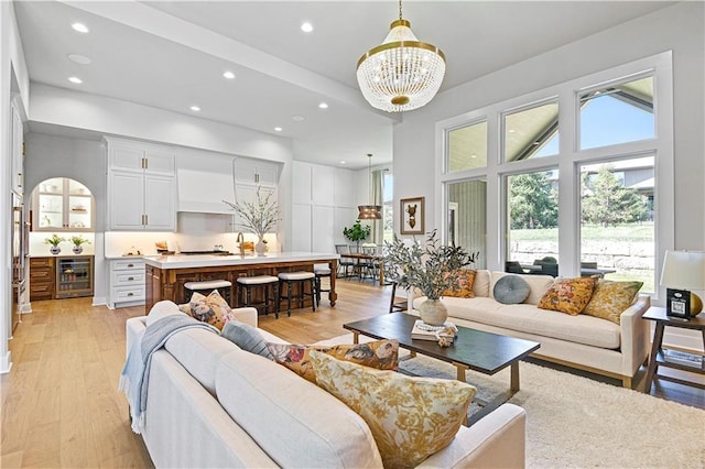 living room featuring beverage cooler, light wood finished floors, recessed lighting, and a notable chandelier