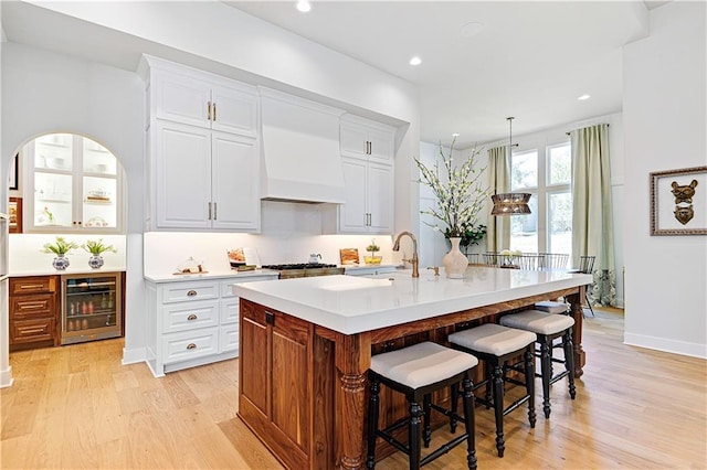 kitchen with beverage cooler, a sink, a kitchen breakfast bar, light wood-style floors, and light countertops