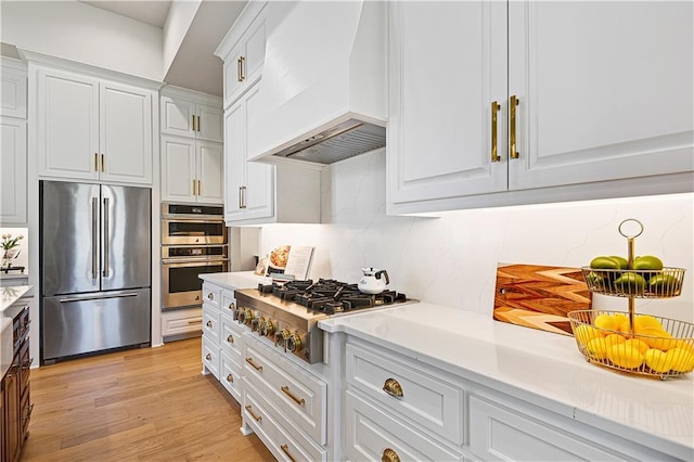 kitchen featuring white cabinets, light countertops, appliances with stainless steel finishes, custom exhaust hood, and light wood finished floors