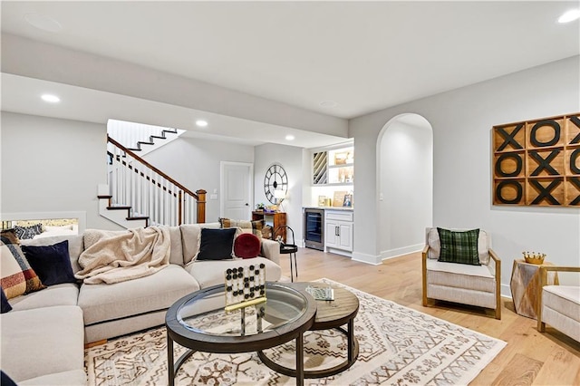 living area with arched walkways, light wood-style flooring, beverage cooler, stairway, and a bar