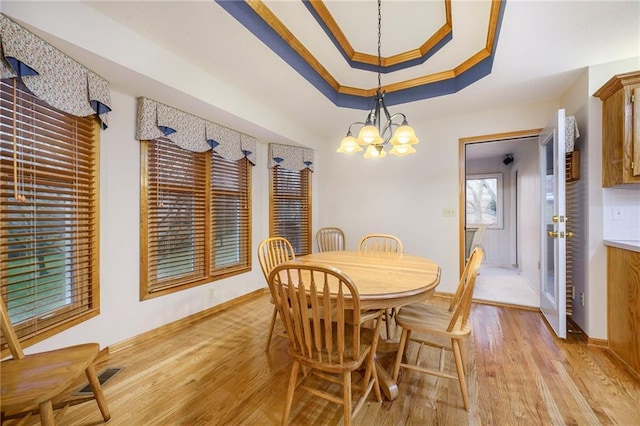 dining room featuring baseboards, ornamental molding, a tray ceiling, light wood-type flooring, and a chandelier