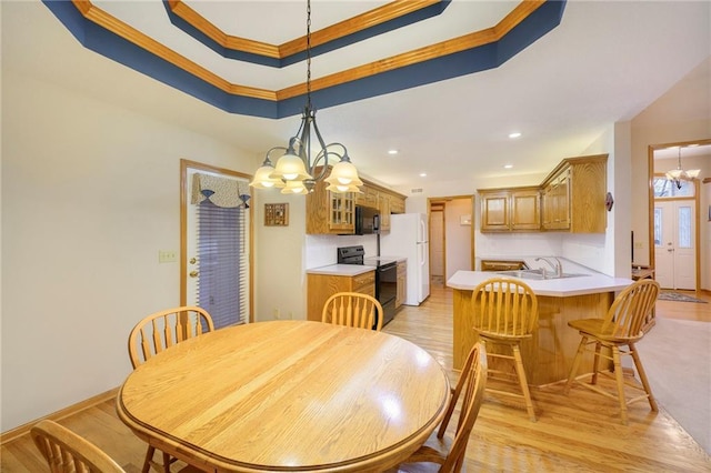 dining space featuring a tray ceiling, crown molding, light wood-style floors, a chandelier, and recessed lighting