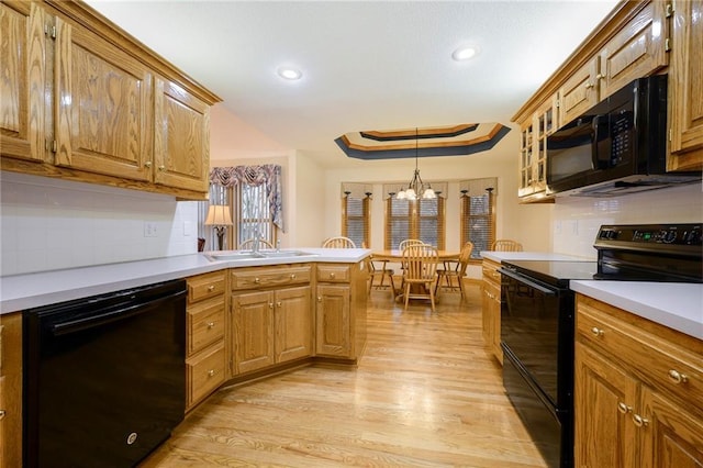 kitchen with a peninsula, light countertops, black appliances, light wood finished floors, and a tray ceiling