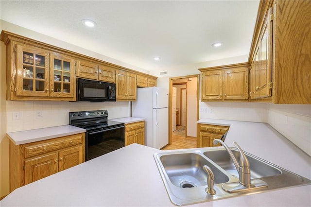 kitchen with light countertops, backsplash, glass insert cabinets, a sink, and black appliances