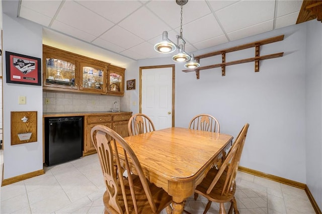 dining area with light tile patterned floors, indoor wet bar, a paneled ceiling, and baseboards