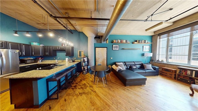 kitchen with light stone countertops, light wood-type flooring, black appliances, a kitchen bar, and a sink