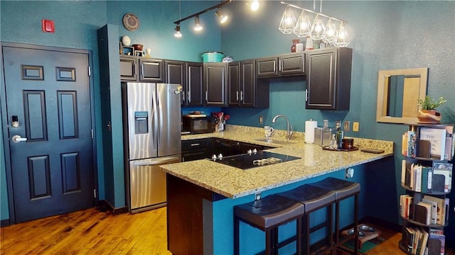 kitchen featuring stainless steel fridge with ice dispenser, a peninsula, black electric cooktop, light wood-style floors, and a sink